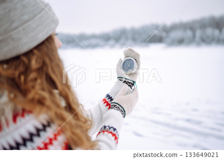 Close-up of a young woman in a hat holding a compass lying in her hand on a mitten. Close-up of a young woman in a hat holding a compass lying in her hand on a mitten. 133649021