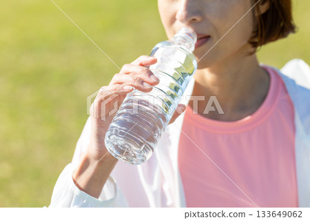 Middle-aged woman drinking bottled water after exercising outdoors Middle-aged woman drinking bottled water after exercising outdoors 133649062
