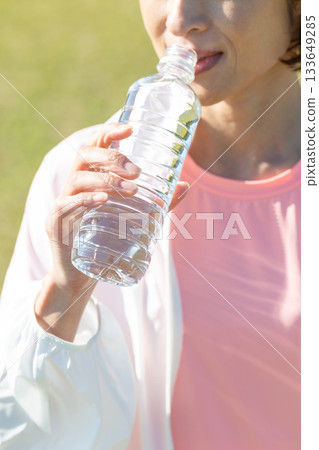 Middle-aged woman drinking bottled water after exercising outdoors Middle-aged woman drinking bottled water after exercising outdoors 133649285