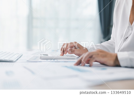 Close up of businesswoman using calculator for financial analysis and accounting on office desk with charts and reports. Concept of business planning, budget calculation and investment strategy. 133649510