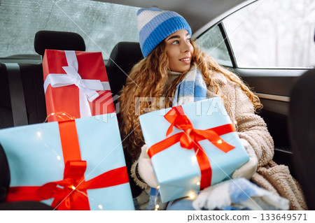 Beautiful young woman with New Year's gifts is riding in back seat of car. Concept of winter holiday Beautiful young woman with New Year's gifts is riding in back seat of car. Concept of winter holiday 133649571