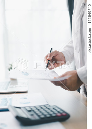A businesswoman reviews financial report while holding documents and pointing with pen at office desk. Concept of accounting, budget management, financial analysis and corporate business planning. 133649740