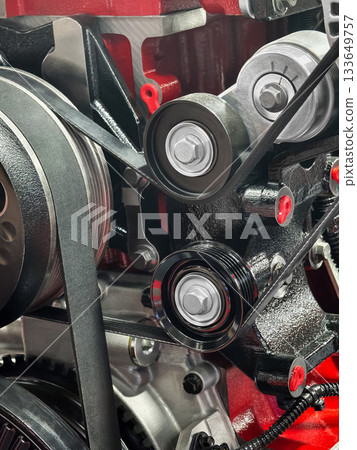 Close-up of a red engine showing pulleys and belts with detailed mechanics in a workshop setting Close-up of a red engine showing pulleys and belts with detailed mechanics in a workshop setting 133649757