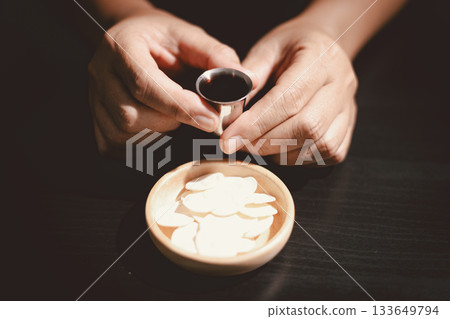 Hands holding communion bread with a wooden bowl and wine cup, symbolizing Holy Communion, the Eucharist, the sacrifice of Jesus Christ and Christian faith in the Lord Supper. 133649794