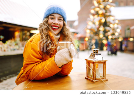 A woman in a bright jacket and red lips walks through a Christmas market and drinks a hot drink. A woman in a bright jacket and red lips walks through a Christmas market and drinks a hot drink. 133649825