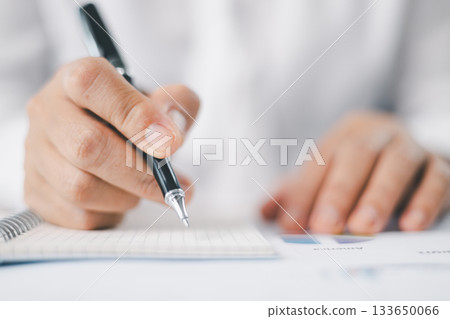 Concept of business planning and financial analysis. A businesswoman writes notes on documents with charts and reports, using laptop and calculator for budget management at modern office desk. 133650066