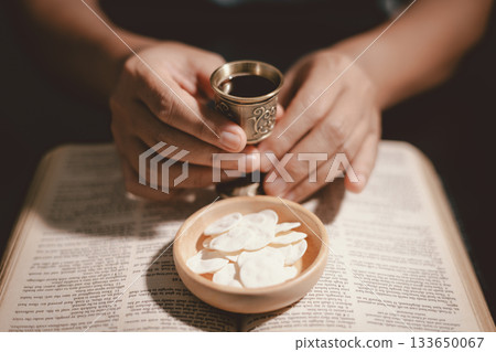 Hands holding communion bread with a wooden bowl and wine cup, symbolizing Holy Communion, the Eucharist, the sacrifice of Jesus Christ and Christian faith in the Lord Supper. 133650067