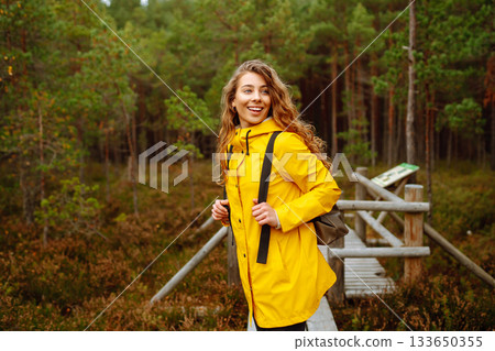 Hiker woman with a backpack hiking on a wooden path in a swamp forest. Active lifestyle Hiker woman with a backpack hiking on a wooden path in a swamp forest. Active lifestyle 133650355