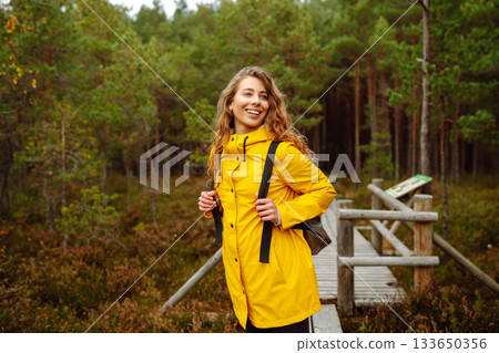 Hiker woman with a backpack hiking on a wooden path in a swamp forest. Active lifestyle 133650356
