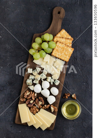 Gourmet cheese platter with crackers, grapes, walnuts, and honey on rustic dark background Gourmet cheese platter with crackers, grapes, walnuts, and honey on rustic dark background 133650596