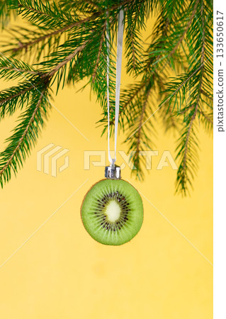Creative christmas ornament: kiwi slice hanging on pine branch for unique holiday decor Creative christmas ornament: kiwi slice hanging on pine branch for unique holiday decor 133650617