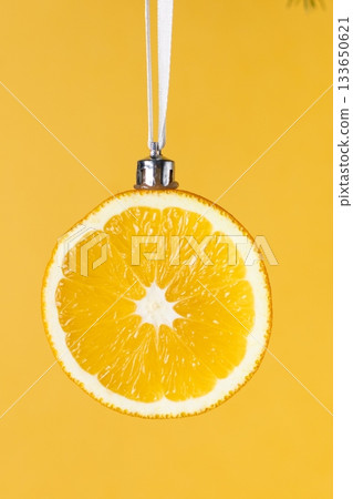 Creative christmas decoration: orange slice ornament hung on pine branch with yellow background Creative christmas decoration: orange slice ornament hung on pine branch with yellow background 133650621