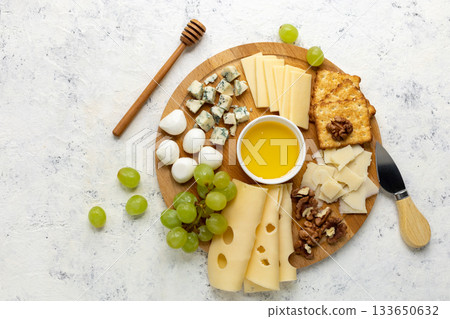 Assorted cheese platter with grapes, honey, and crackers on wooden board 133650632