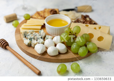 Assorted cheese platter with grapes, honey, and crackers on wooden board Assorted cheese platter with grapes, honey, and crackers on wooden board 133650633