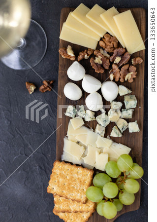 Gourmet cheese and wine pairing with crackers, grapes, and nuts on rustic board 133650643