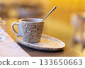 Rustic ceramic coffee cup with spoon on matching saucer in cozy setting 133650663