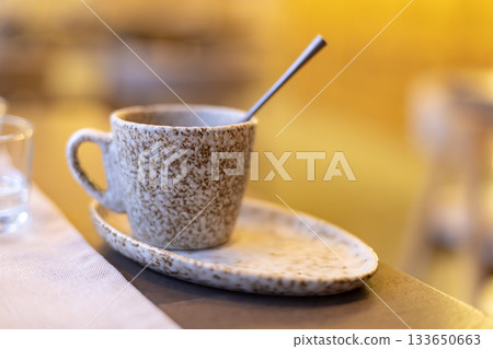 Rustic ceramic coffee cup with spoon on matching saucer in cozy setting 133650663