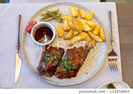 Grilled steak with roasted potatoes, dipping sauce, and pickles on a rustic plate 133650665