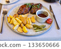 Grilled steak with roasted potatoes, dipping sauce, and pickles on a rustic plate 133650666