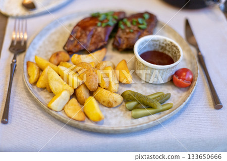 Grilled steak with roasted potatoes, dipping sauce, and pickles on a rustic plate 133650666