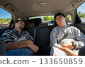 Berlin, Germany, August 10, 2023. Car travel concept: two young people have fallen sound asleep in the back seat. Travel lifestyle, freedom, and relaxation. 133650859