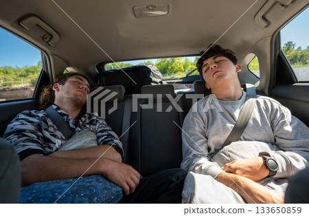 Berlin, Germany, August 10, 2023. Car travel concept: two young people have fallen sound asleep in the back seat. Travel lifestyle, freedom, and relaxation. 133650859