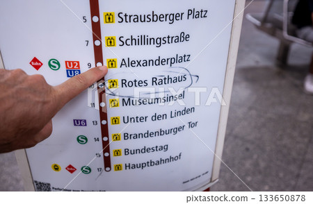 Berlin, Germany, August 10, 2023. On the subway, a hand points to the Alexanderplatz stop on the information board. Lifestyle using public transportation. 133650878