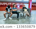 Berlin, Germany, August 10, 2023. A subway station in Frankfurt am Main, characterized by its red and orange tiled walls. On a bench, two young men and a middle-aged woman wait for the train to pass. 133650879