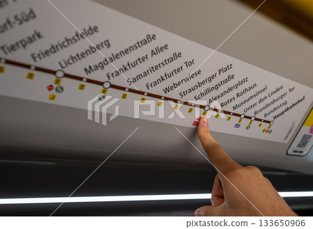 Berlin, Germany, August 10, 2023. On the subway, a hand points to the Alexanderplatz stop on the information board. Lifestyle using public transportation. 133650906