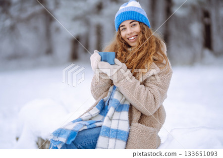 Smiling woman with a thermos in a snowy forest enjoying nature. Adventure concept. Lifestyle. 133651093
