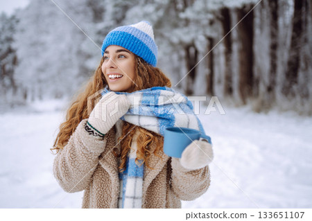Smiling woman with a thermos in a snowy forest enjoying nature. Adventure concept. Lifestyle. 133651107