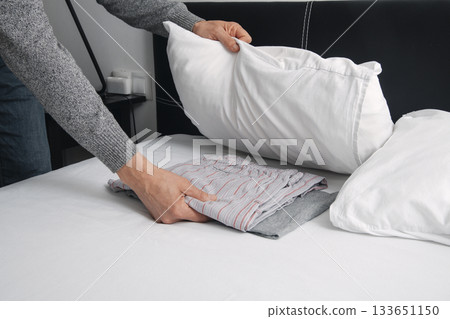 a man tucks his pajamas under his pillow a man tucks his pajamas under his pillow 133651150