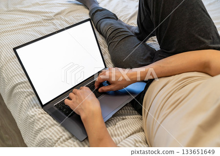 man lying in bed while watching on laptop. 133651649