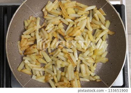 Potatoes cut into slices are deliciously fried in a frying pan. 133651900