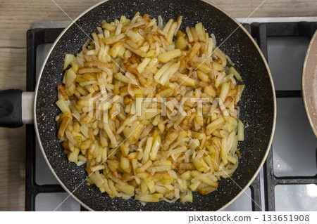 Sliced potatoes with onions are deliciously fried in a frying pan. 133651908