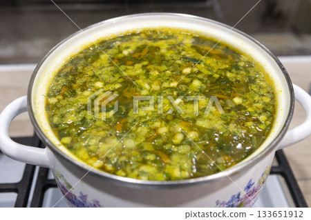 Fresh vegetable soup is boiling in a saucepan, hot steam rises up 133651912