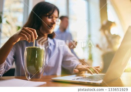 Young woman working on laptop while stirring matcha in bright workspace 133651929