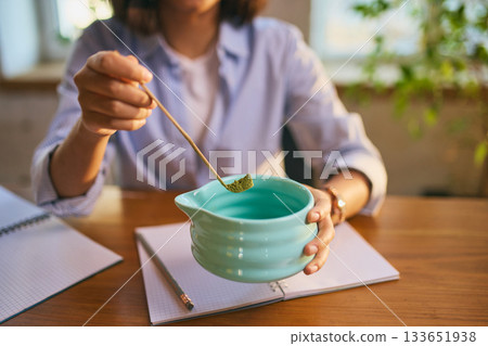 Young woman measuring matcha powder at desk with notebooks during calm preparation Young woman measuring matcha powder at desk with notebooks during calm preparation 133651938