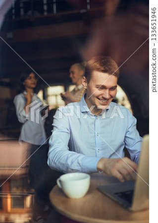 Man working on a laptop in a cafe with coworkers chatting in the background Man working on a laptop in a cafe with coworkers chatting in the background 133651946