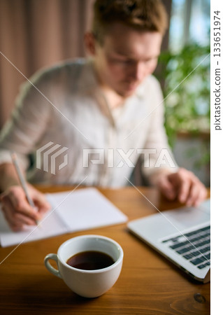 Coffee cup on desk as man writes notes and works in office 133651974