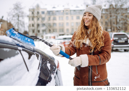 Young woman cleaning snow from car with brush. Transport, winter, people and vehicle concept. Young woman cleaning snow from car with brush. Transport, winter, people and vehicle concept. 133652112