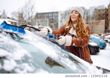 Young woman cleaning snow from car with brush. Transport, winter, people and vehicle concept. Young woman cleaning snow from car with brush. Transport, winter, people and vehicle concept. 133652116