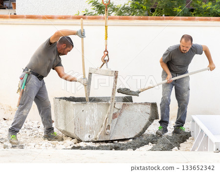Pouring fresh ready-mixed concrete from wheelbarrow on floor during for construction of a house Pouring fresh ready-mixed concrete from wheelbarrow on floor during for construction of a house 133652342