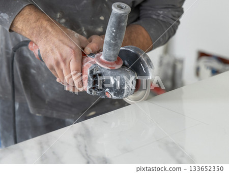 Craftman in grey shirt cuts a gray marble tile using an angle grinder. Handy men at work, hands closeup 133652350