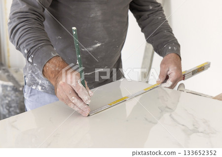 Craftman in grey shirt measures a marble tile using a ruler. Handy men at work, hands closeup 133652352