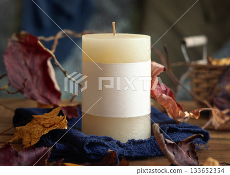 Candle with a label near autumn dried leaves closeup,  fall mockup in blue, red and orange 133652354