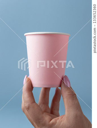 Female hand with disposable pink paper cup against light blue closeup, mockup, copy space Female hand with disposable pink paper cup against light blue closeup, mockup, copy space 133652360