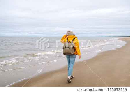 Attractive woman on windy cold beach. Beautiful tourist woman in stylish clothes enjoys life by sea. Attractive woman on windy cold beach. Beautiful tourist woman in stylish clothes enjoys life by sea. 133652819