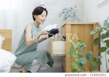 一位女士正在把衣服放進衣櫃裡 一位女士正在把衣服放進衣櫃裡 133652831