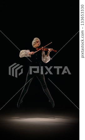 Violinist captured mid-jump playing expressive classical lines on dark stage. Violinist captured mid-jump playing expressive classical lines on dark stage. 133653330